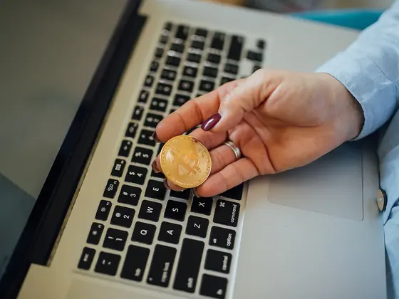 Hand holding a gold bitcoin token over a laptop keyboard